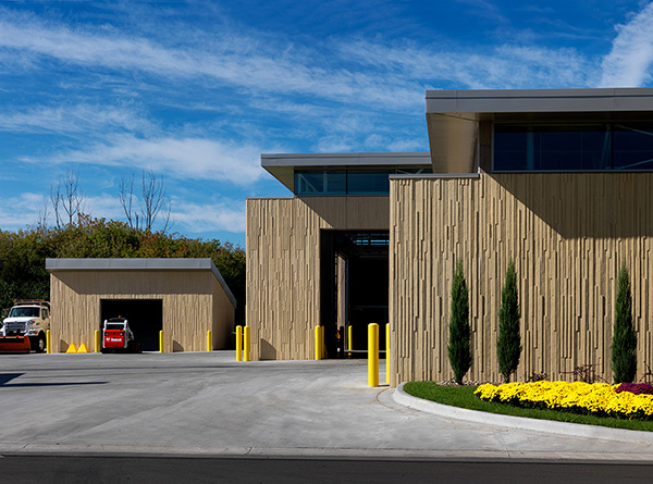 Locally-sourced precast concrete resembles wood planks on the north- and south-facing walls. This image shows vehicle entry to the larger maintenance area (right) and a stand-alone storage garage (left).