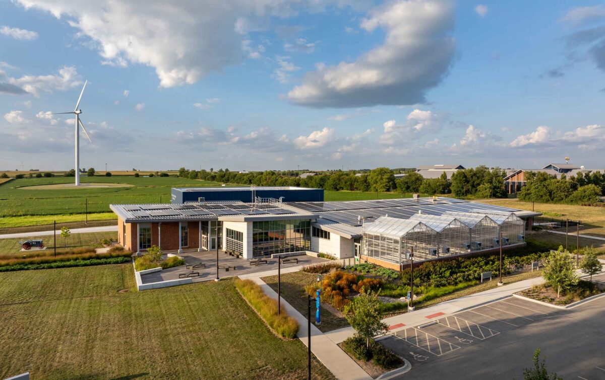 Aerial view of agriculture facility with wind turbine, solar panels, and greenhouses
