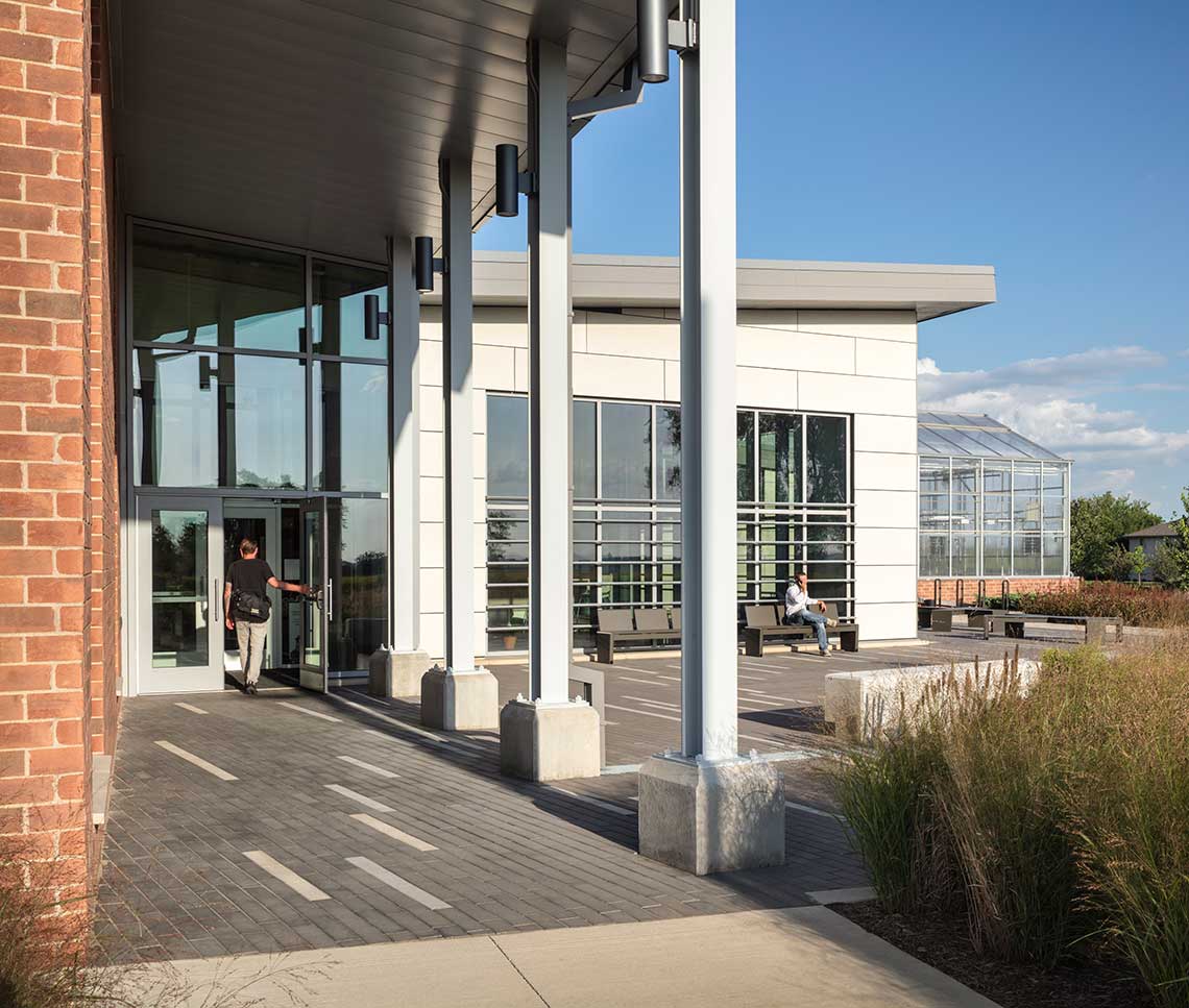 College student walking under canopy toward building with greenhouse in background