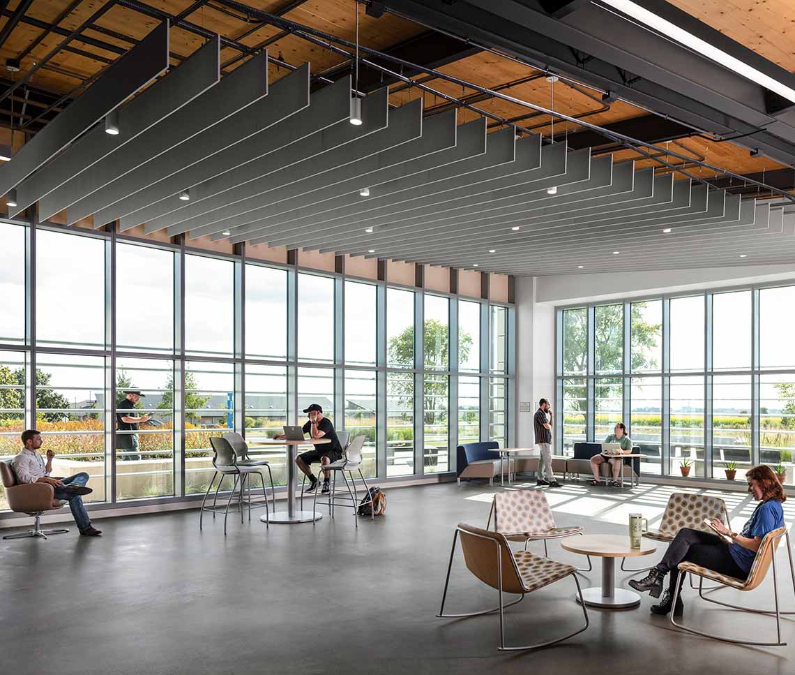 College students in gathering area with large windows, different seating types, and decorative ceiling