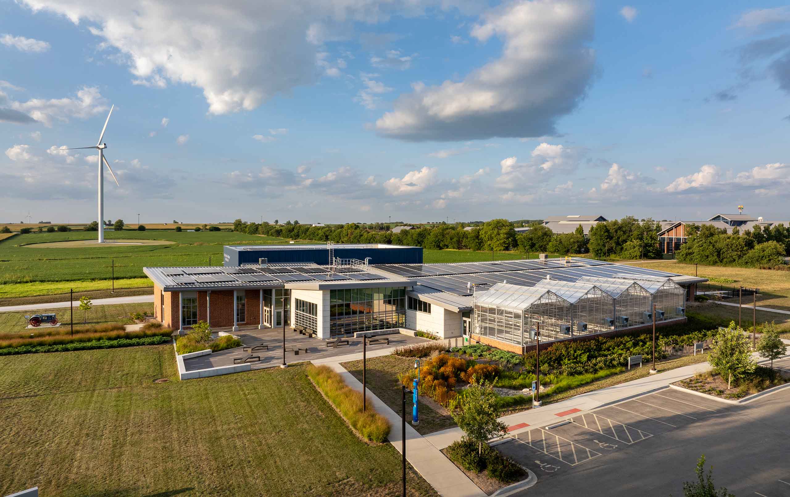 Aerial view of agriculture facility with wind turbine, solar panels, and greenhouses