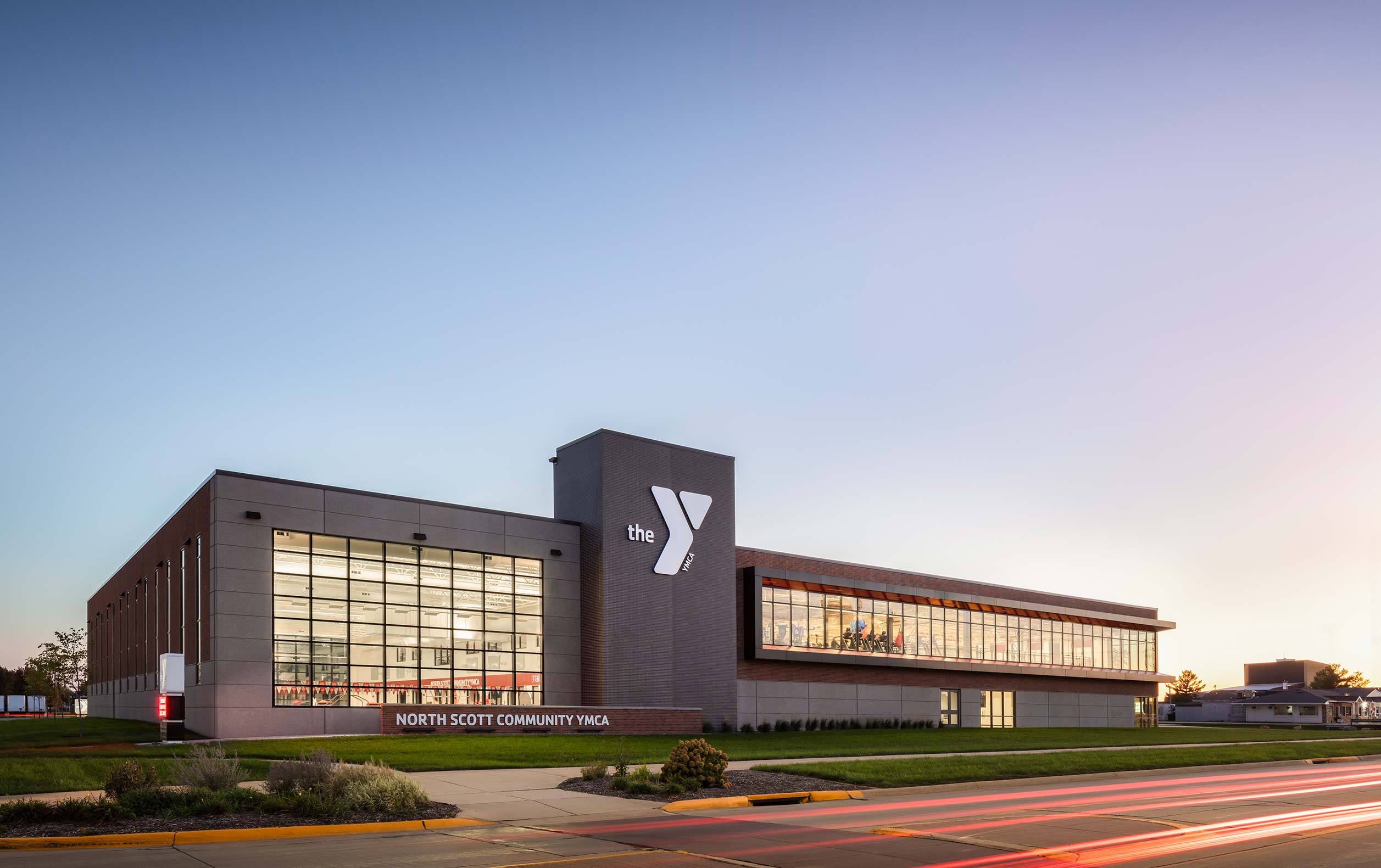 North Scott YMCA exterior dusk photo with view through window into fitness areas