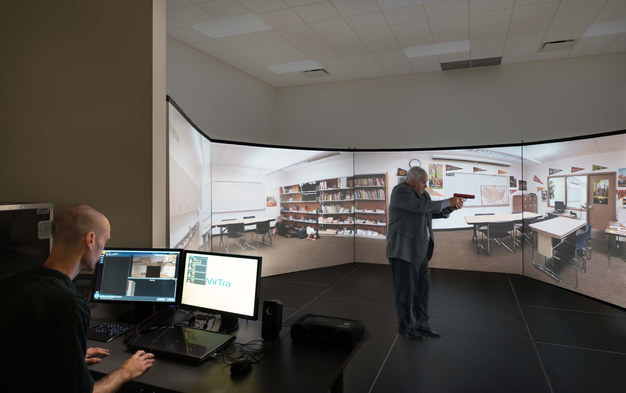 Man operating computer and man holding guy facing screen in video simulation zone at College of DuPage Homeland Security Training Center