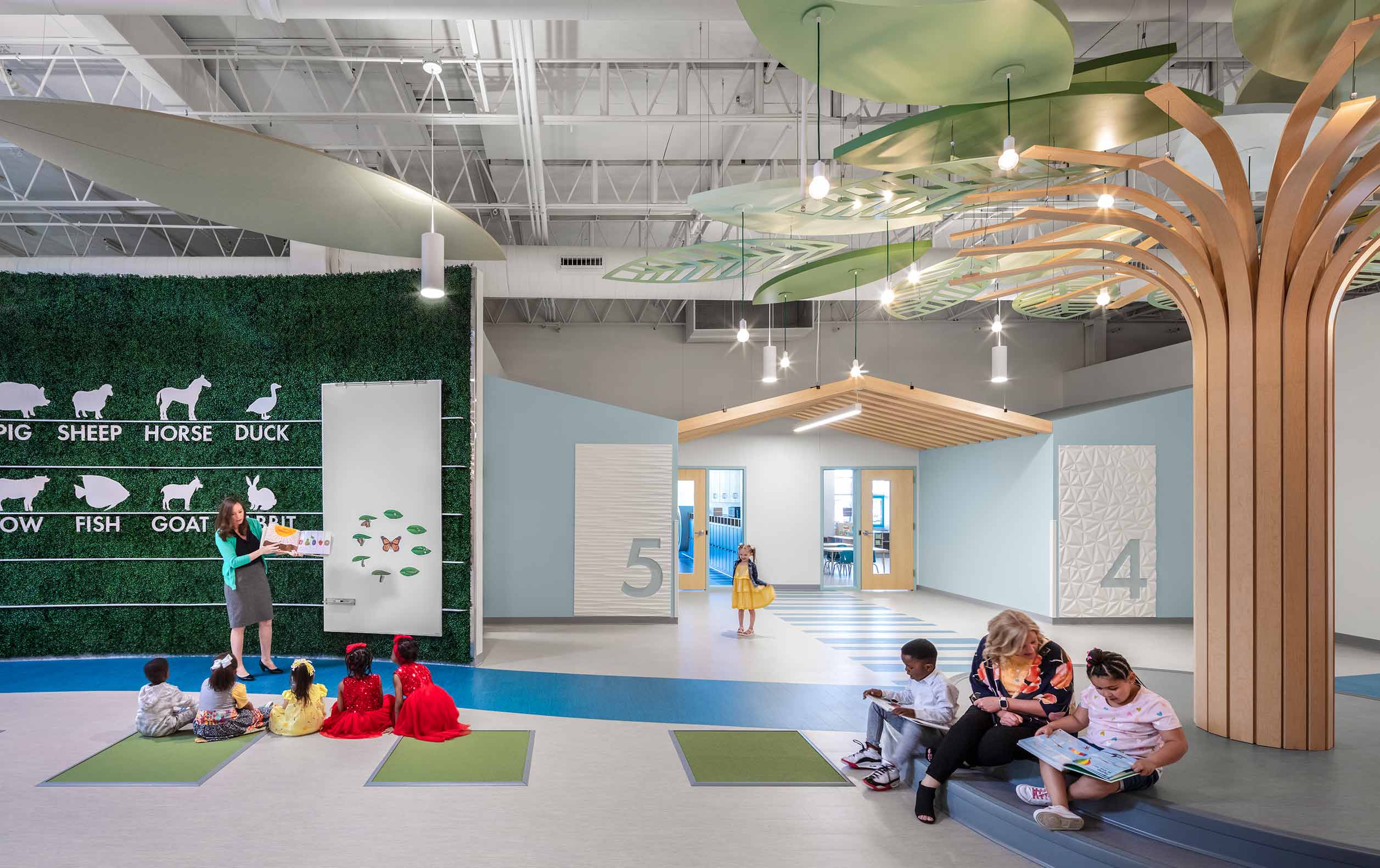 Preschool with groups of students sitting around teachers in open area with column that looks like a tree