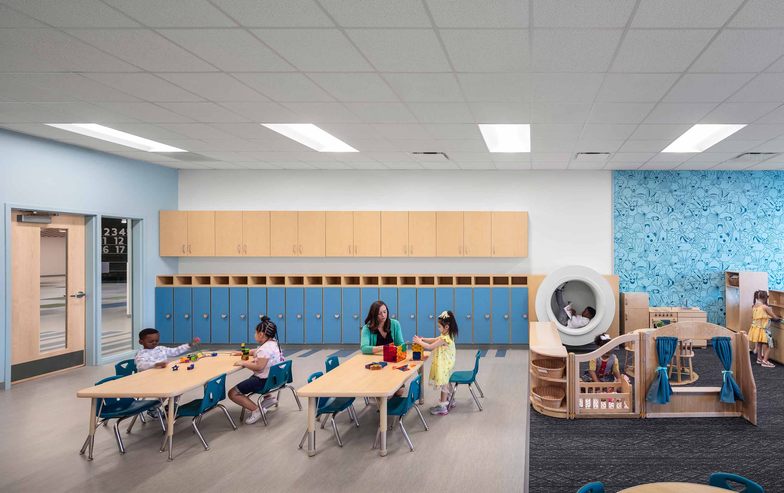 Preschool classroom with teacher and students, and student sitting in hole built into wall