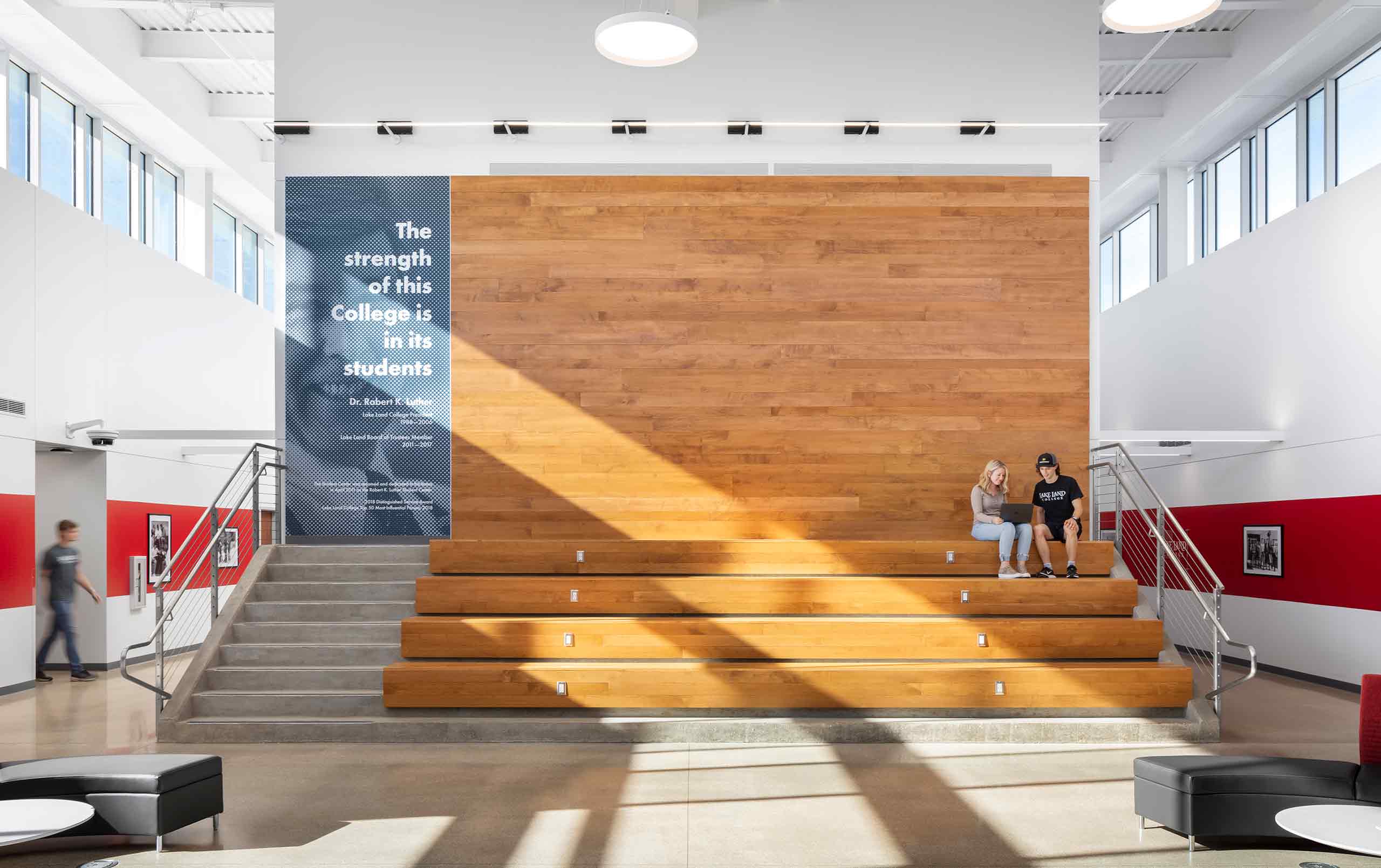 Students sitting on steps leading to wood feature wall