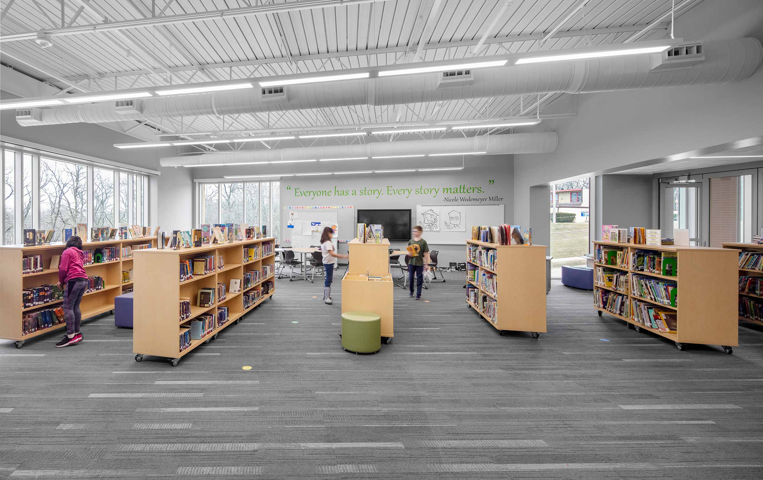 Elementary school library with students, small bookshelves, and views of trees