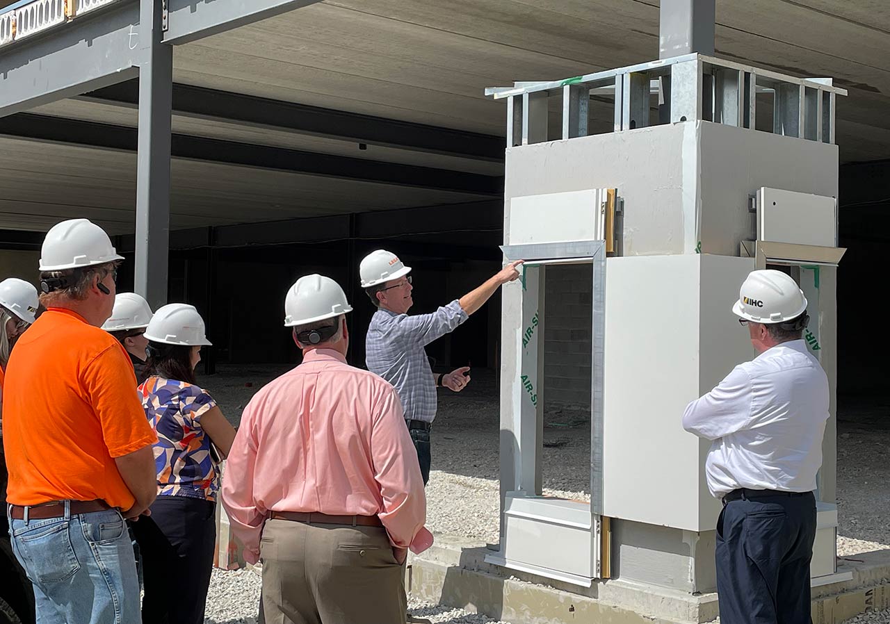 Group of people in construction helmets listening to architect discuss building component at construction site