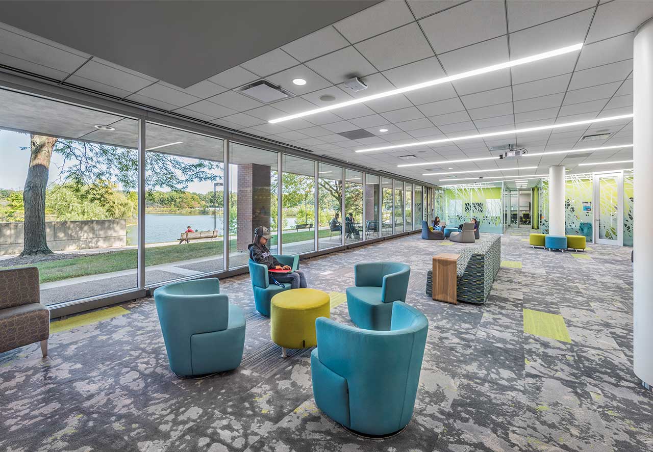 College students in colorful student center with windows displaying trees and lake