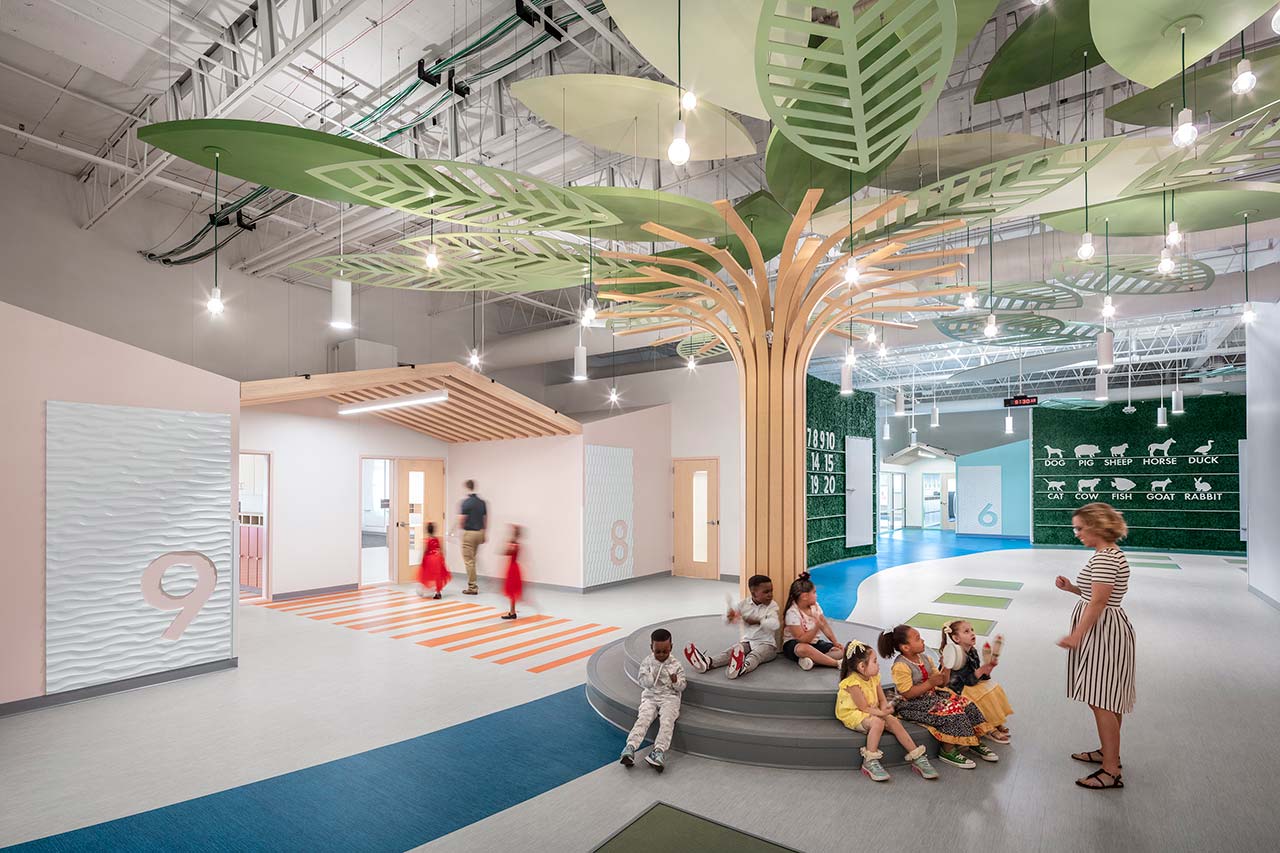 Corridor space with teacher/children underneath learning tree in foreground and students entering classroom in background