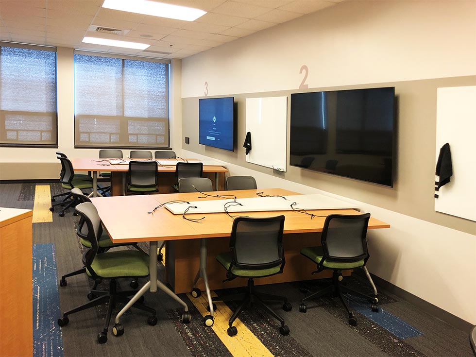 Classroom with "pods" consisting of tables and chairs on casters, as well as a wall-mounted monitor for each pod