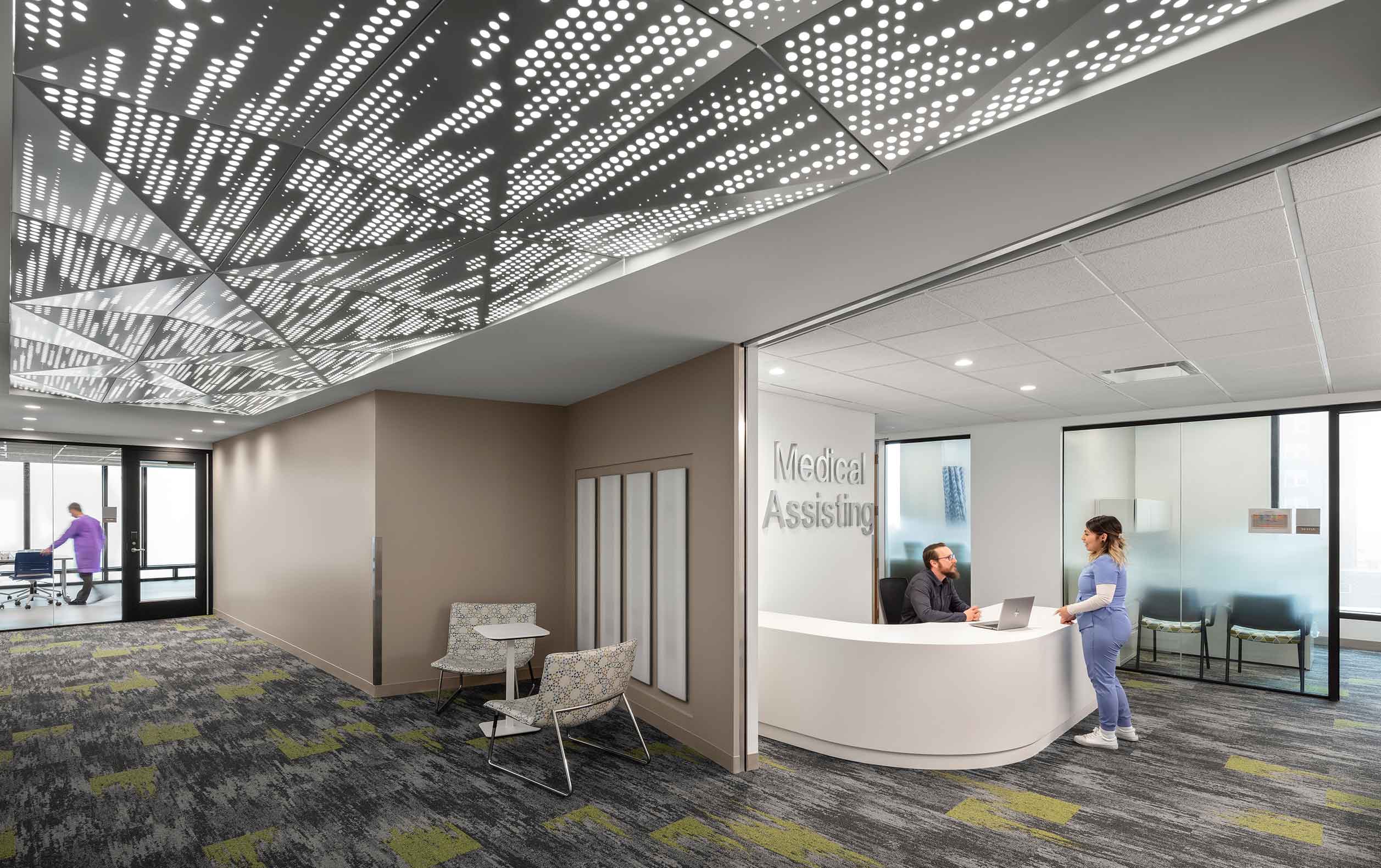 Higher education medical assisting program corridor with people at reception desk and perforated metal ceiling with lights