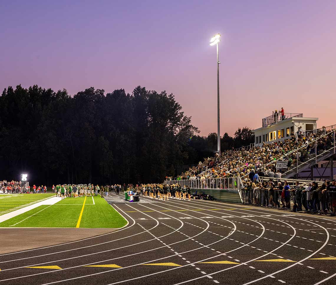 Nighttime view of high school football field and track with fans in the bleachers