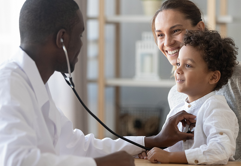 Doctor holding stethoscope to smiling child held by smiling mother