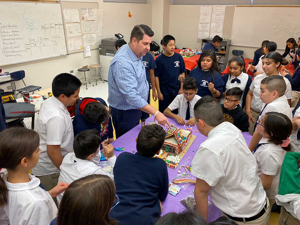 Architect pointing at gingerbread house and surrounded by elementary students