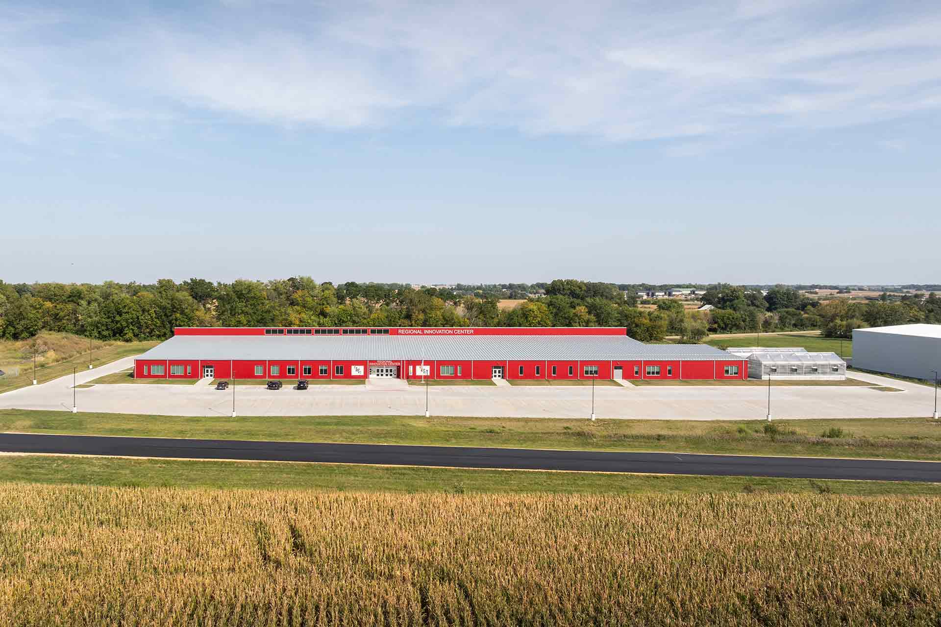 Aerial view of Regional Innovation Center with red metal siding and greenhouses, with agricultural field in foreground