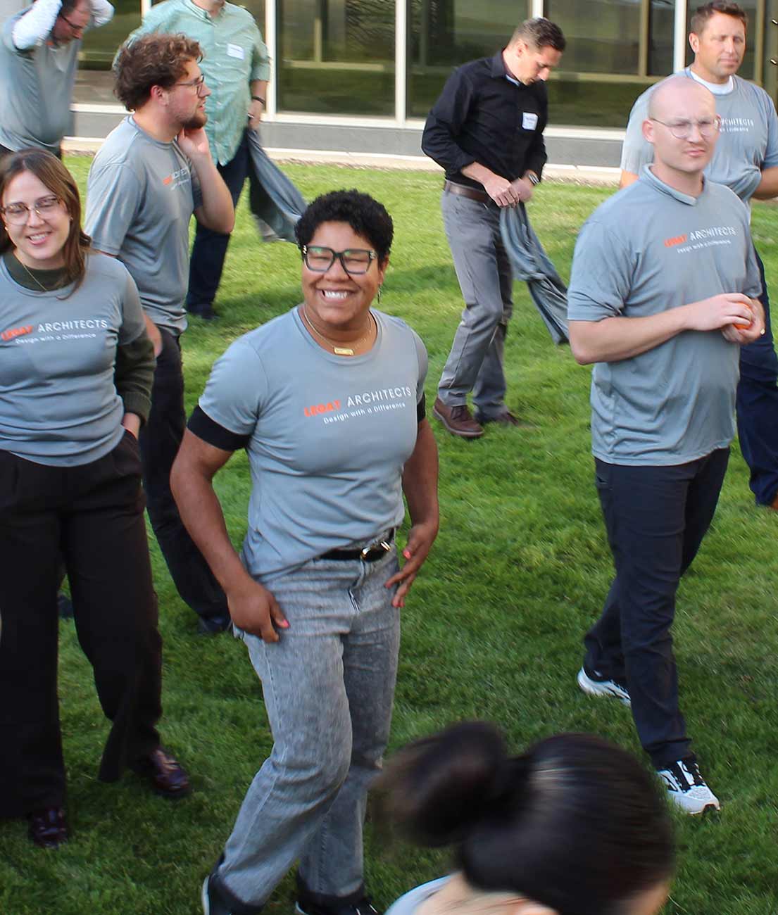 Team members wearing matching Legat Architects shirts enjoy outdoor activities together on the lawn.