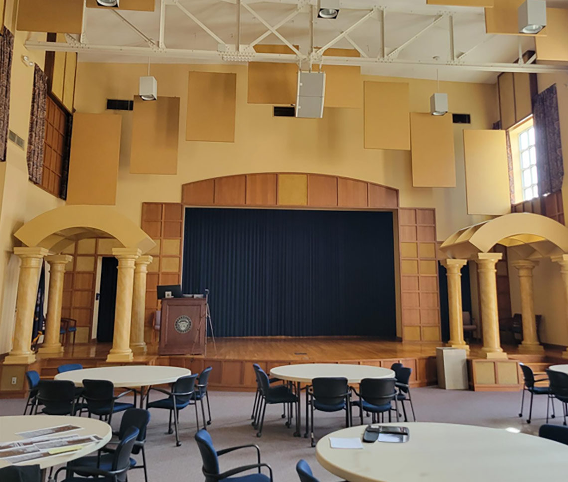 Dated college auditorium with columns and wood panels around stage