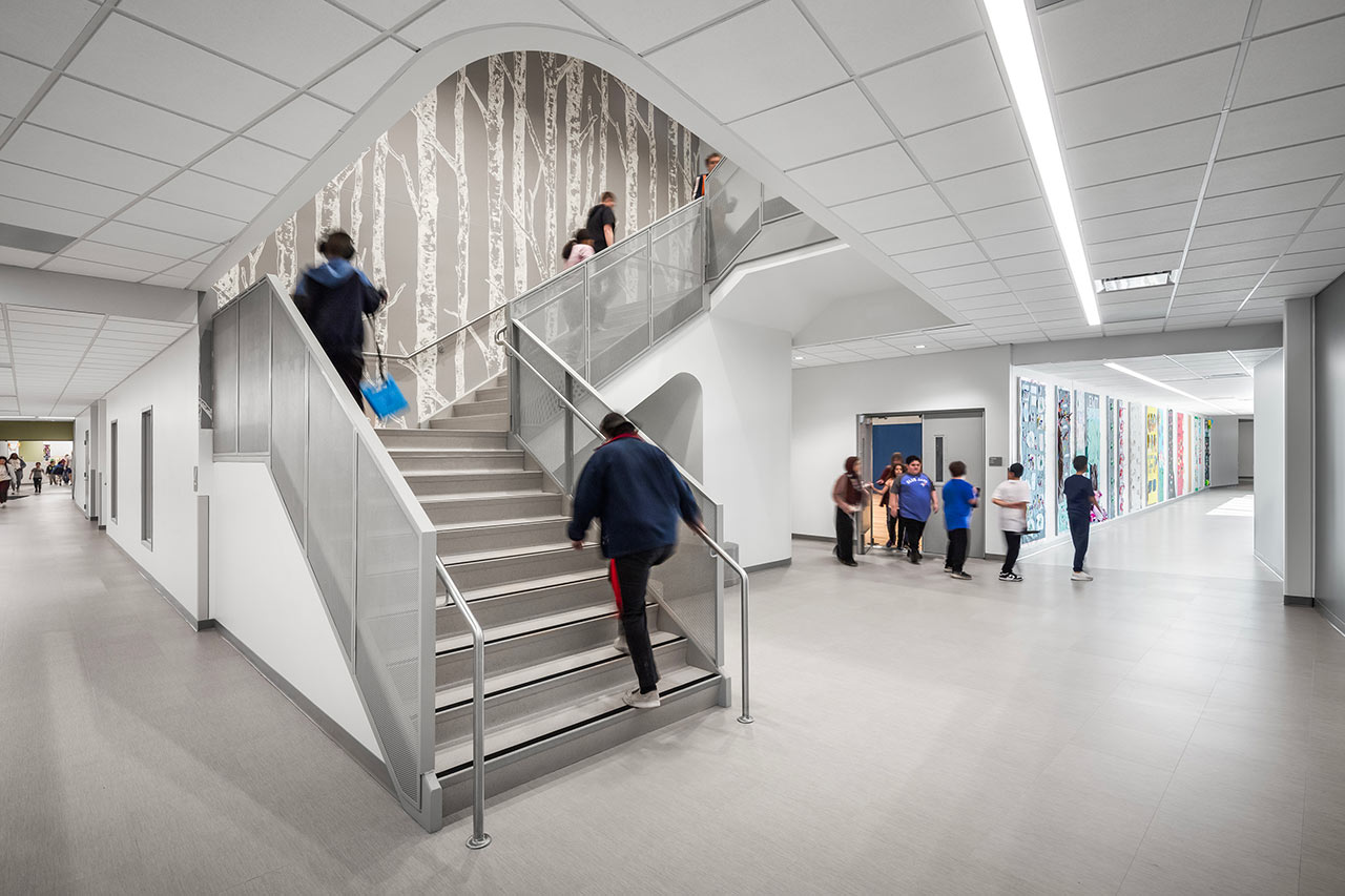 Special education school atrium with staircase, gray and white color scheme, and birch tree wall graphic