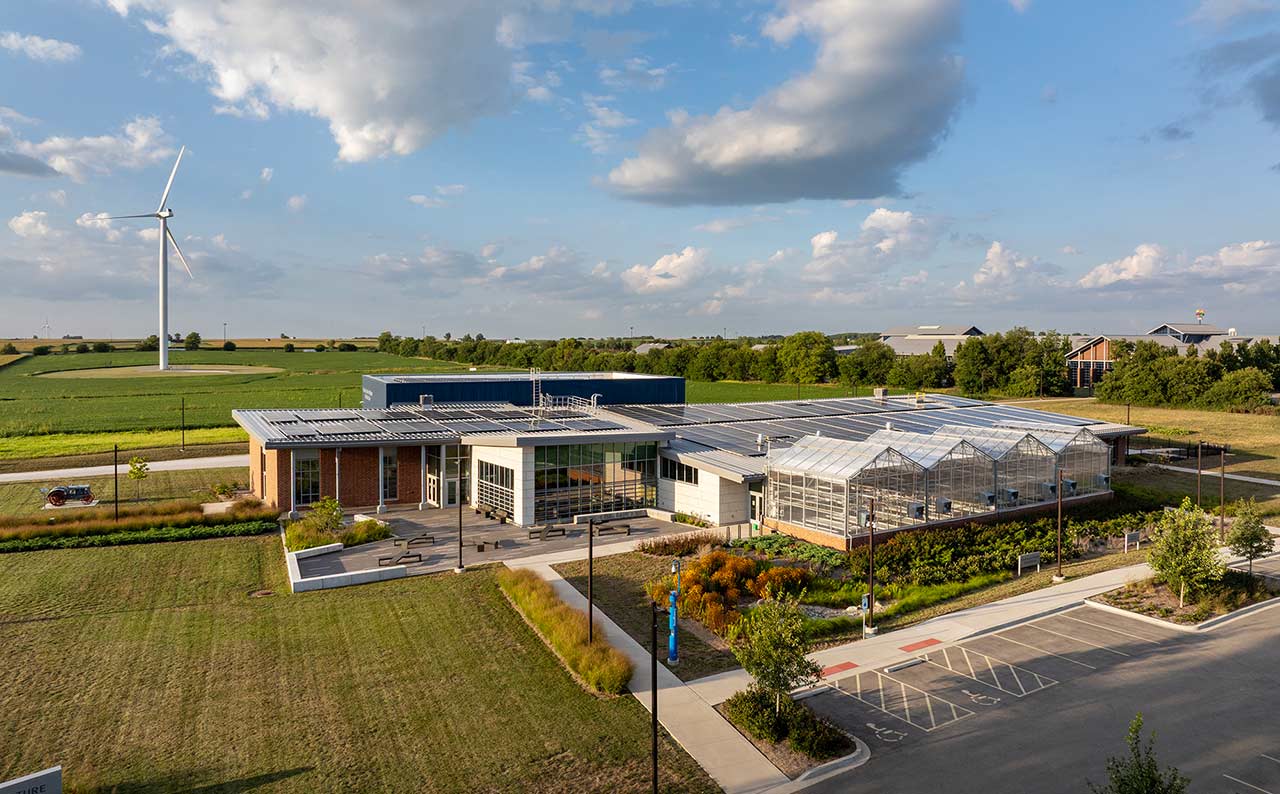 Aerial view of agriculture complex showing farmland, wind turbine, and solar panels