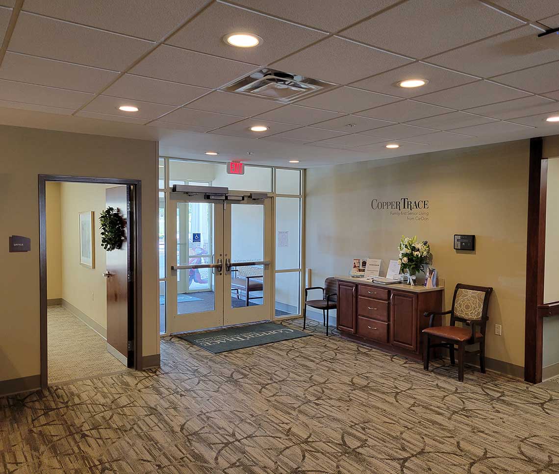 Copper Trace by CarDon senior living entrance lobby before renovation, with dated finishes, older furnishings, and a traditional reception area