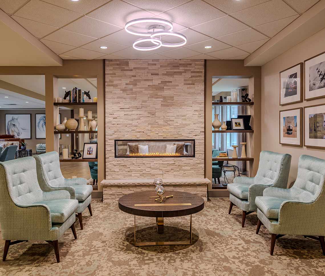 Renovated Copper Trace by CarDon senior living lounge featuring a modern stone fireplace, updated seating, contemporary lighting, and refreshed décor.