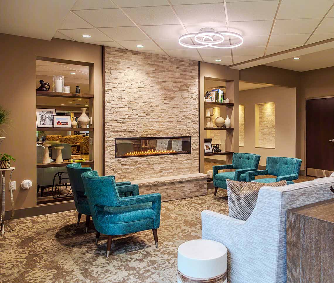 Renovated Copper Trace by CarDon senior living gathering area featuring a modern stone fireplace, teal lounge seating, contemporary lighting, and refreshed finishes.