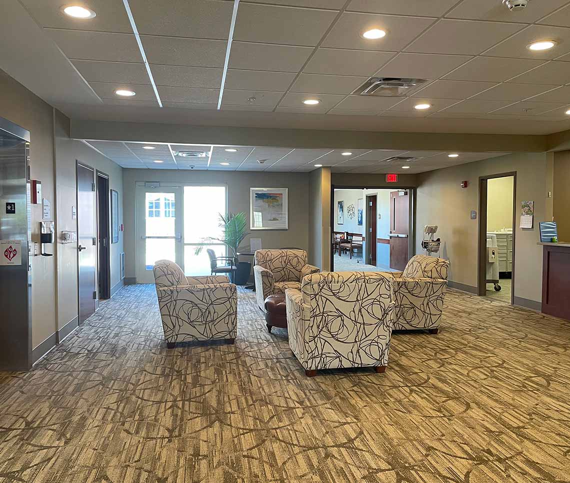 Outdated Copper Trace by CarDon senior living gathering area before renovation, featuring dated patterned carpet, bulky upholstered seating, and older finishes.