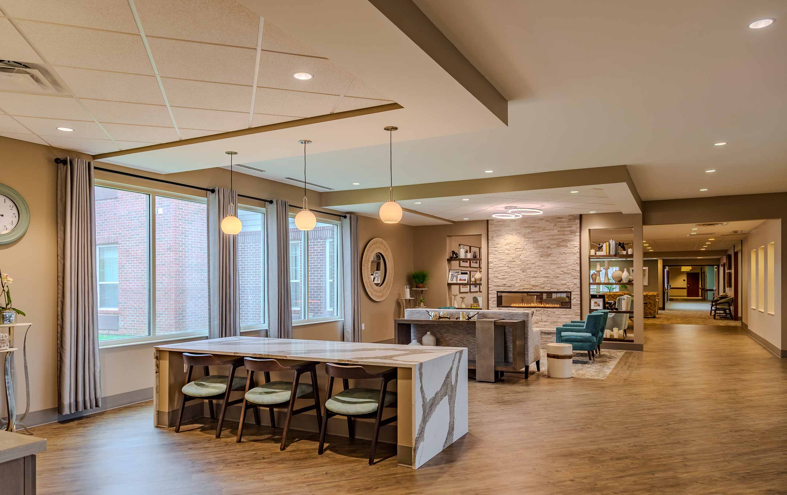 Renovated Copper Trace by CarDon senior living common area featuring a modern stone fireplace, quartz gathering table, updated flooring, contemporary lighting, and open lounge seating.