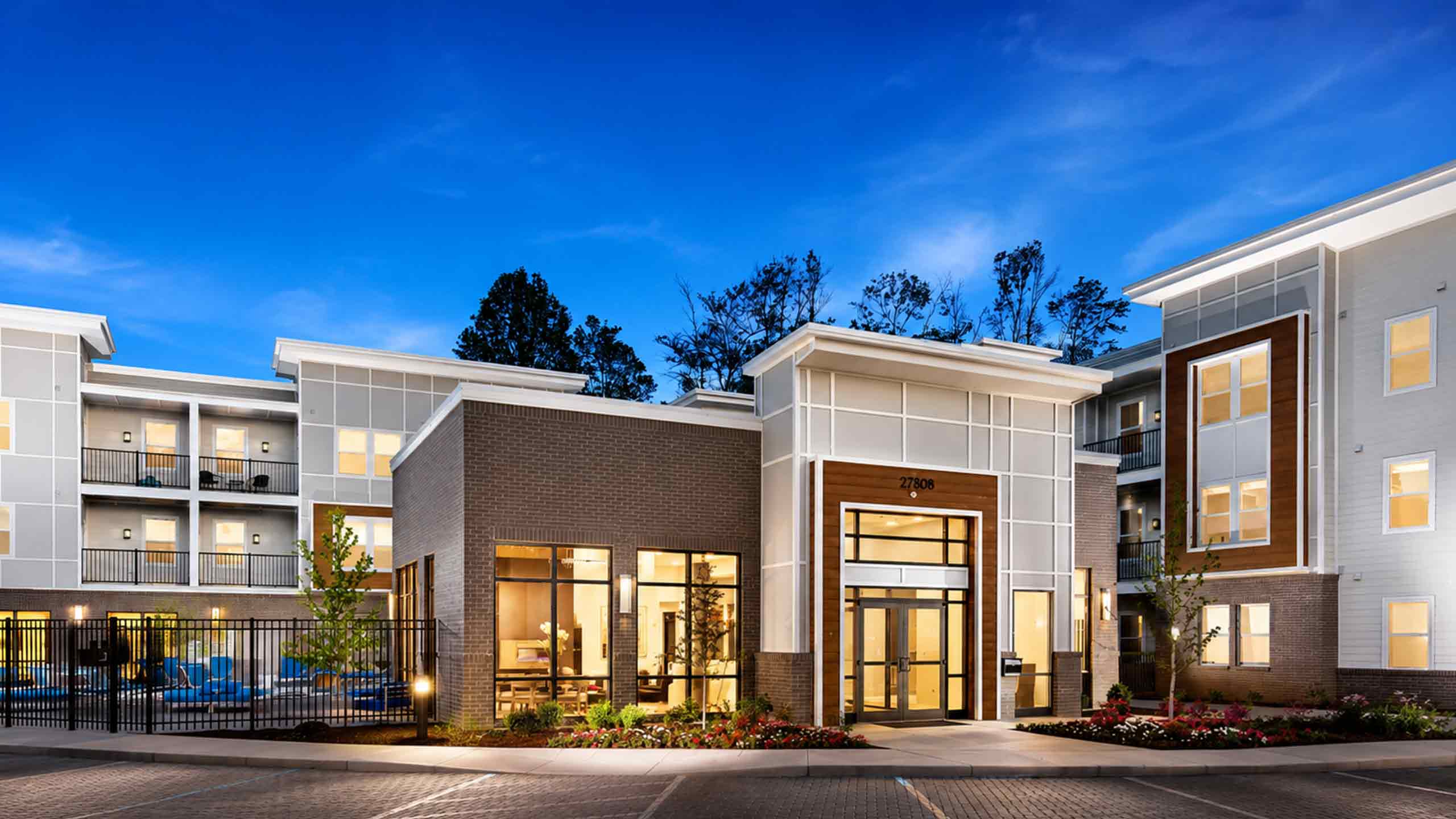 Exterior view of a modern multi-story apartment building and clubhouse exterior under a clear dusk sky.