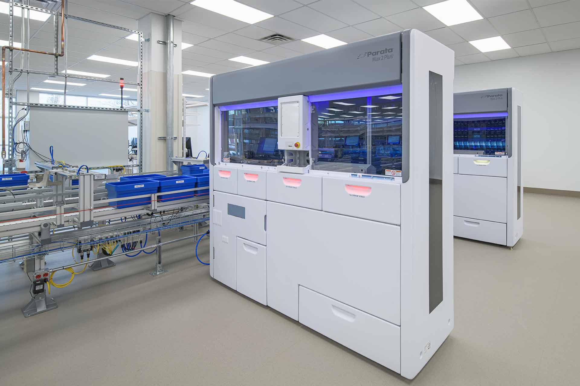 Automated laboratory storage system with blue bins on conveyors in a clean, modern pharmaceutical facility.