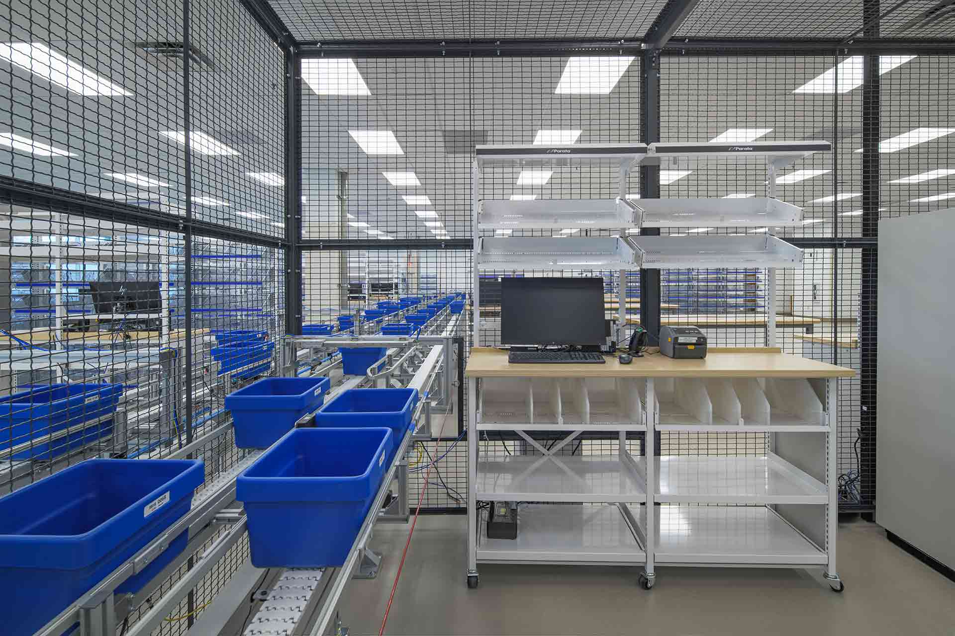 Automated conveyor system with blue bins and workstation inside a secure pharmaceutical fulfillment facility.