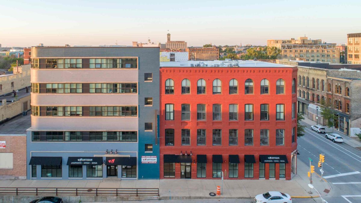 Aerial view of a modern mixed-use apartment building alongside a bright red brick exterior in an urban city setting.
