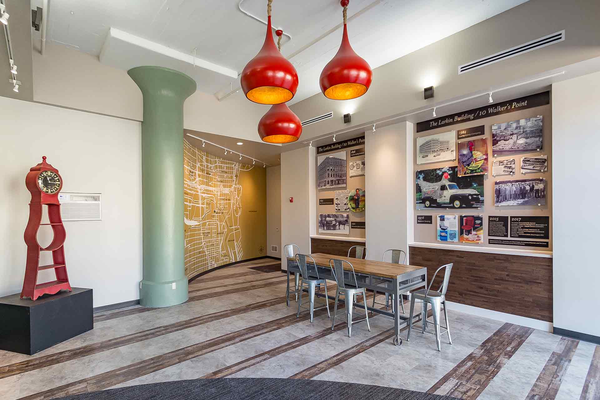 Modern lobby featuring red teardrop pendant lights, a communal table, a green column, and a history wall display.