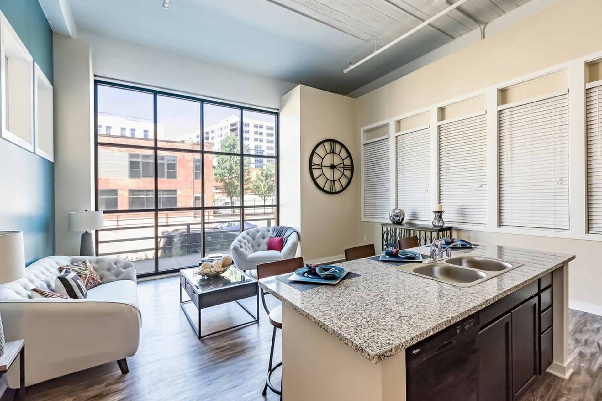 Open-plan apartment layout featuring a kitchen island with granite countertops adjacent to a bright, modern living room.