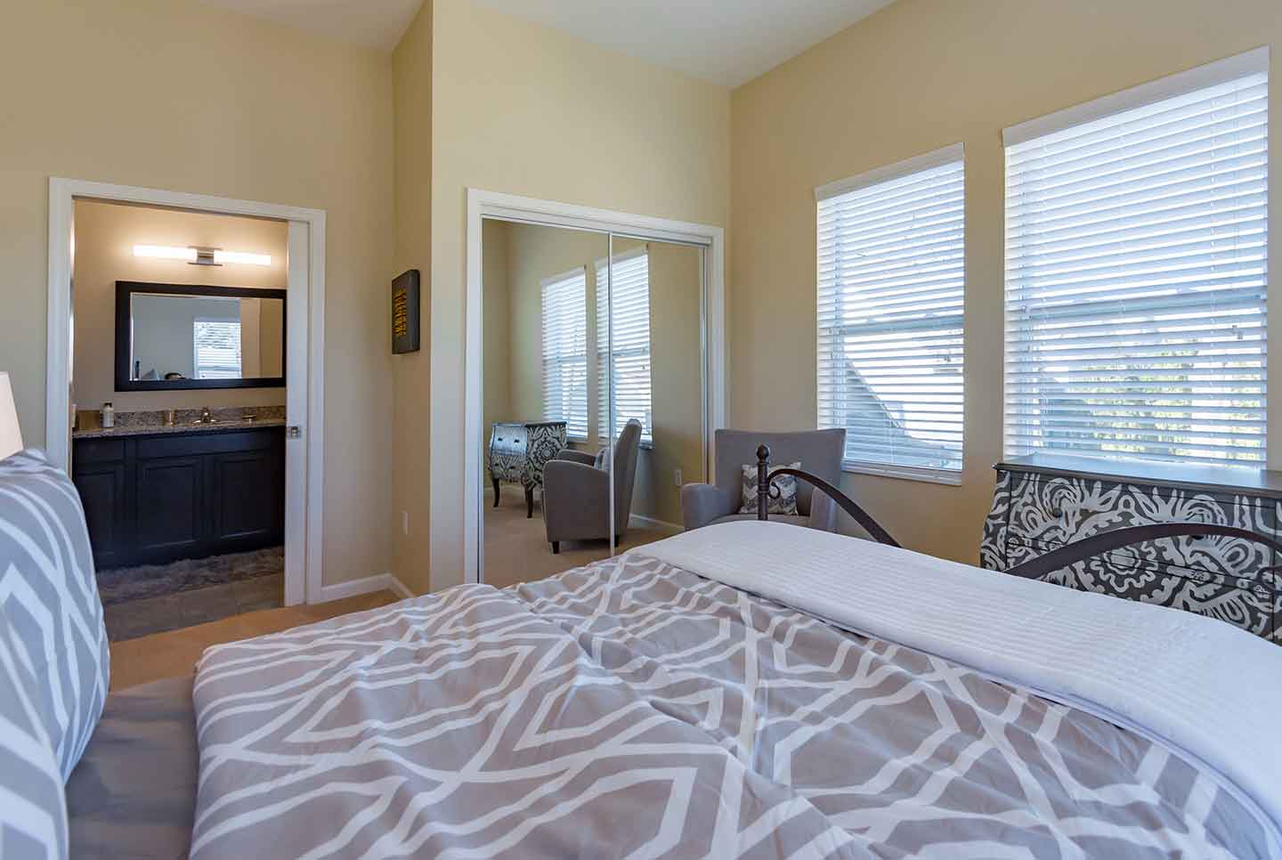 Modern apartment bedroom featuring a patterned bedspread, mirrored closet doors, and an en-suite bathroom view.
