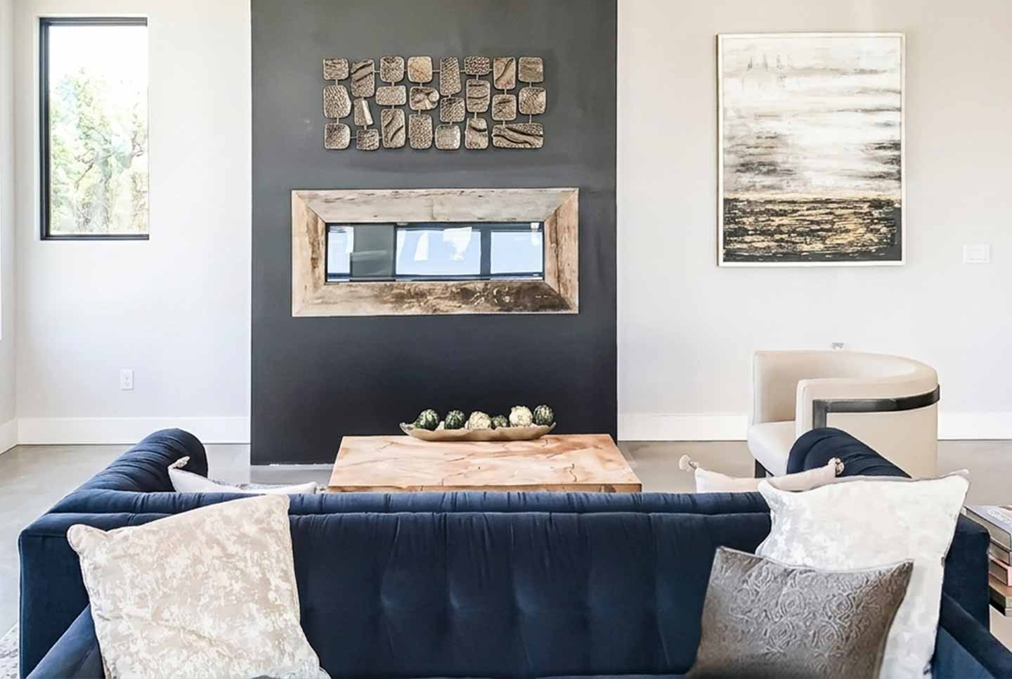 Modern living room lounge featuring a dark accent wall with an embedded fireplace and a dark blue velvet sofa.
