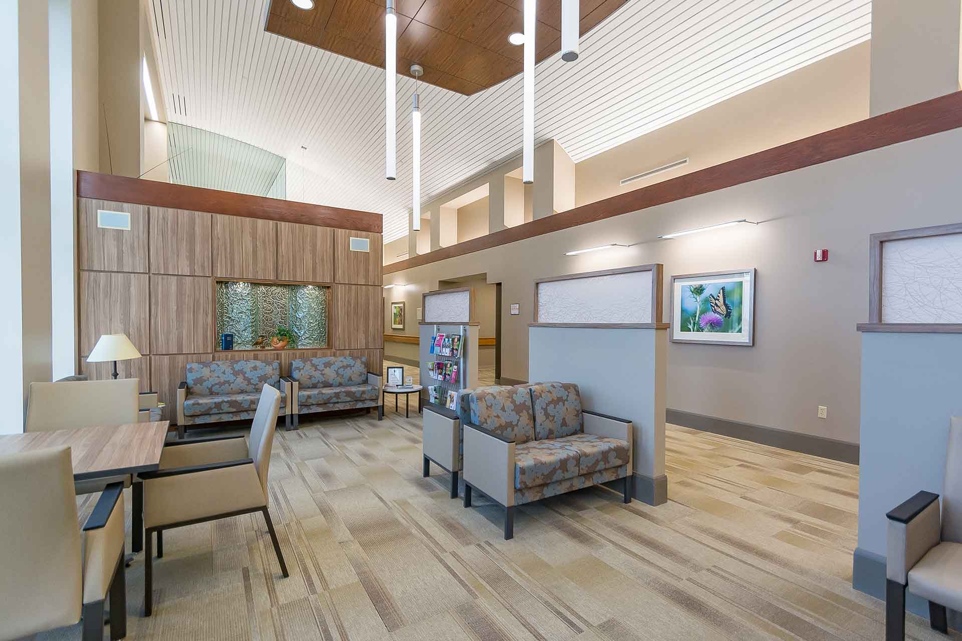 Modern healthcare waiting area with comfortable seating, high ceilings, pendant lighting, and warm wood accents.