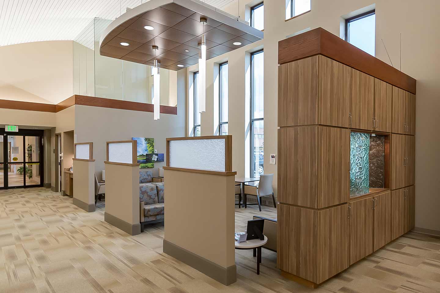 Modern healthcare waiting area with seating alcoves, high ceilings, large windows, and warm wood finishes.