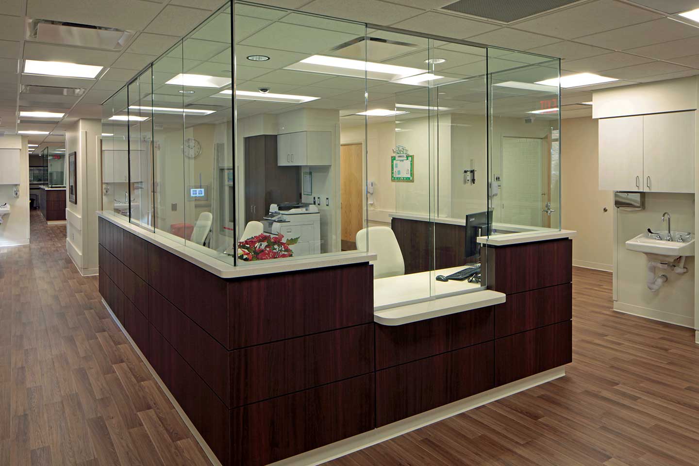 Modern hospital nurses' station with glass partitions, workspaces, and nearby patient care rooms.