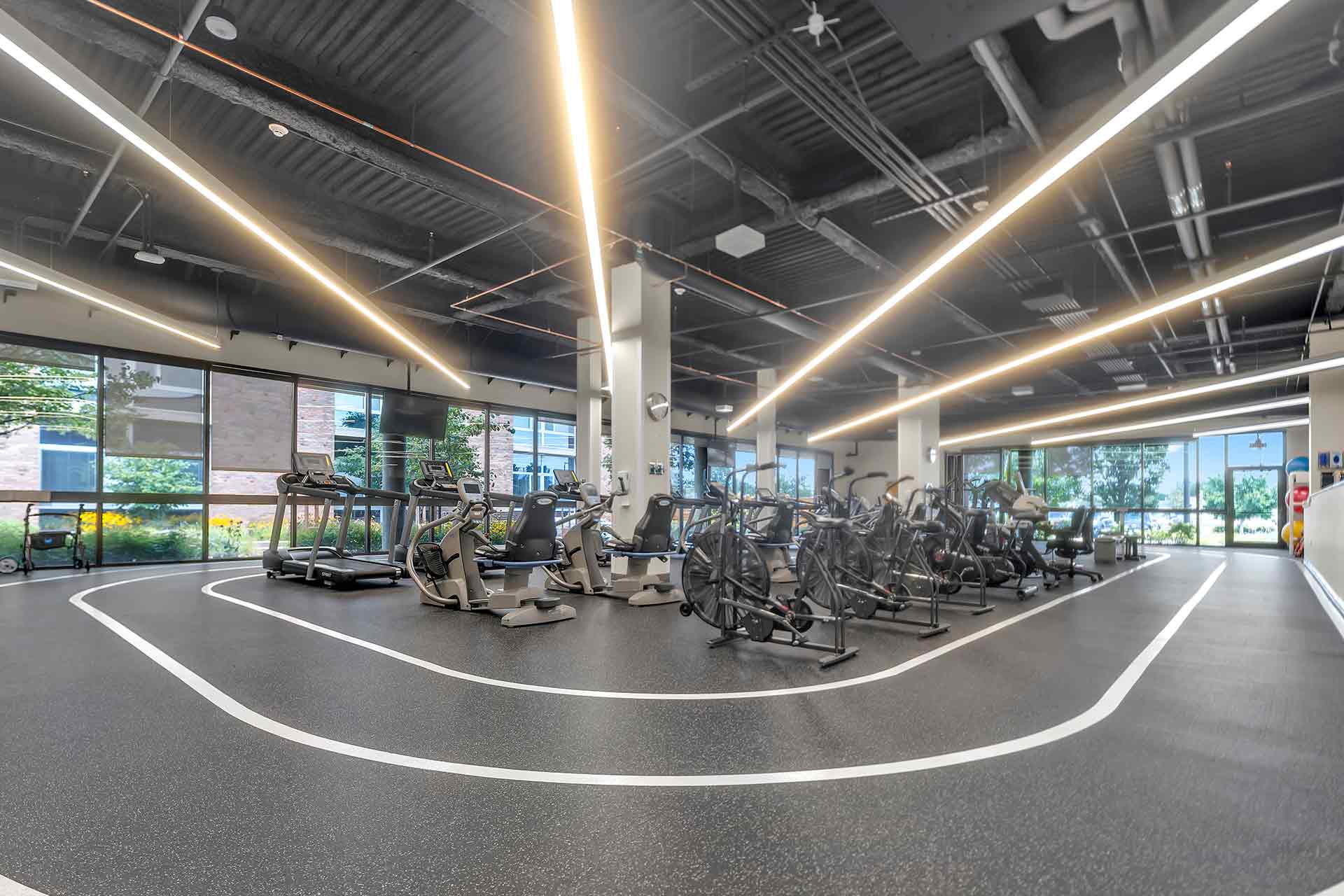 Spacious cardiac rehabilitation gym with treadmills, exercise bikes, and walking track in a bright facility.
