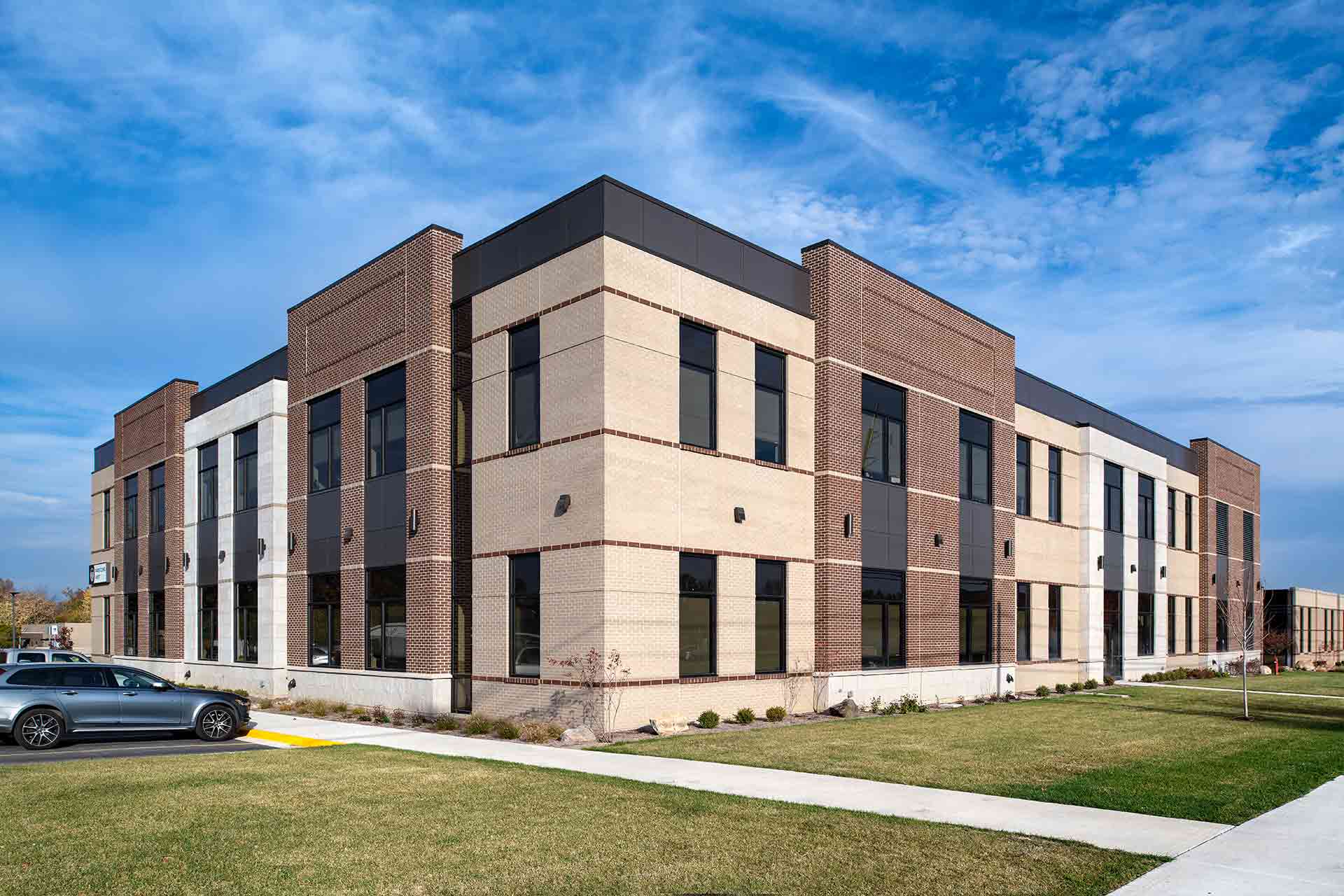 Modern two-story healthcare facility with brick exterior, large windows, landscaped grounds, and blue sky backdrop.
