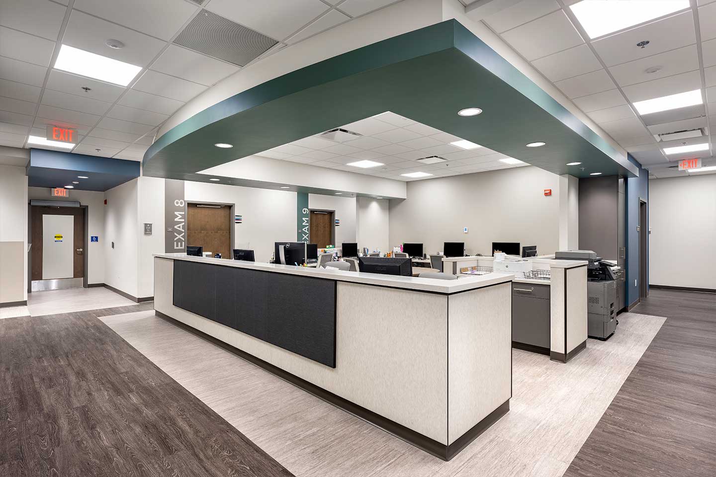 Modern healthcare reception desk with exam room entrances, staff workstations, and bright, open clinical space.