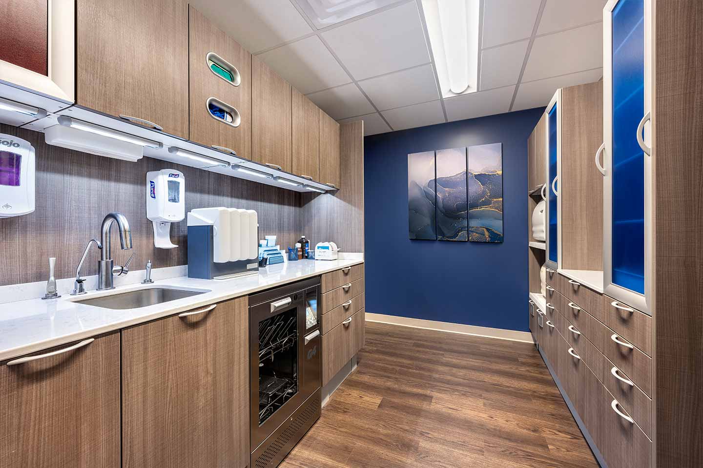 Dental sterilization room featuring wood cabinetry, medical equipment, a sink, and a blue accent wall.