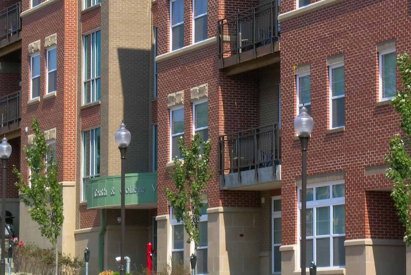Close-up exterior of Tenth and College Village brick apartment building with balconies and street lamps.