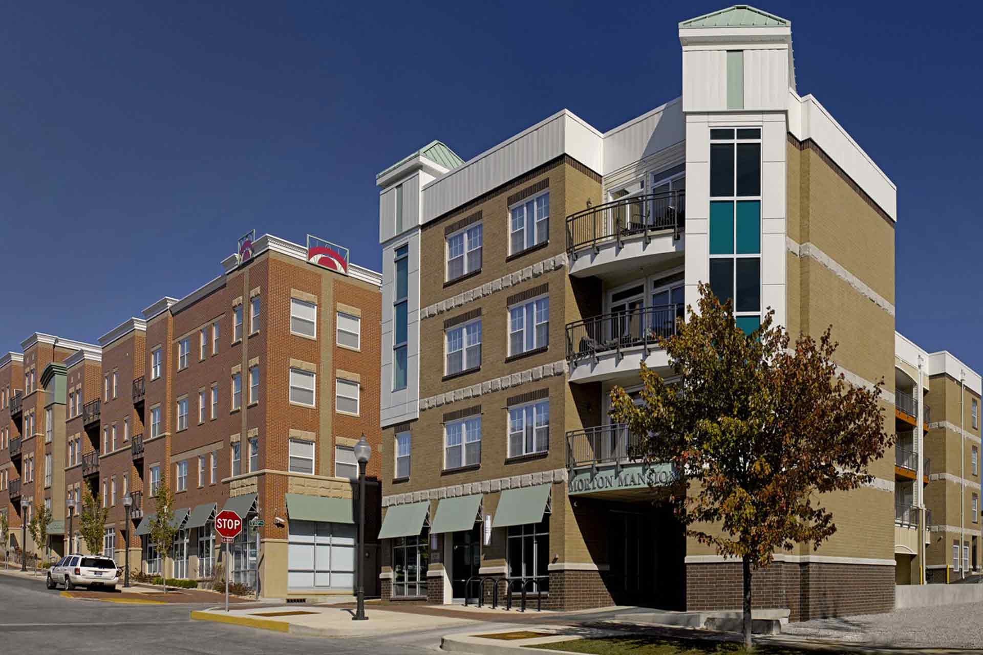 Exterior view of a multi-story modern brick apartment building named Morton Mansion along a street corner.