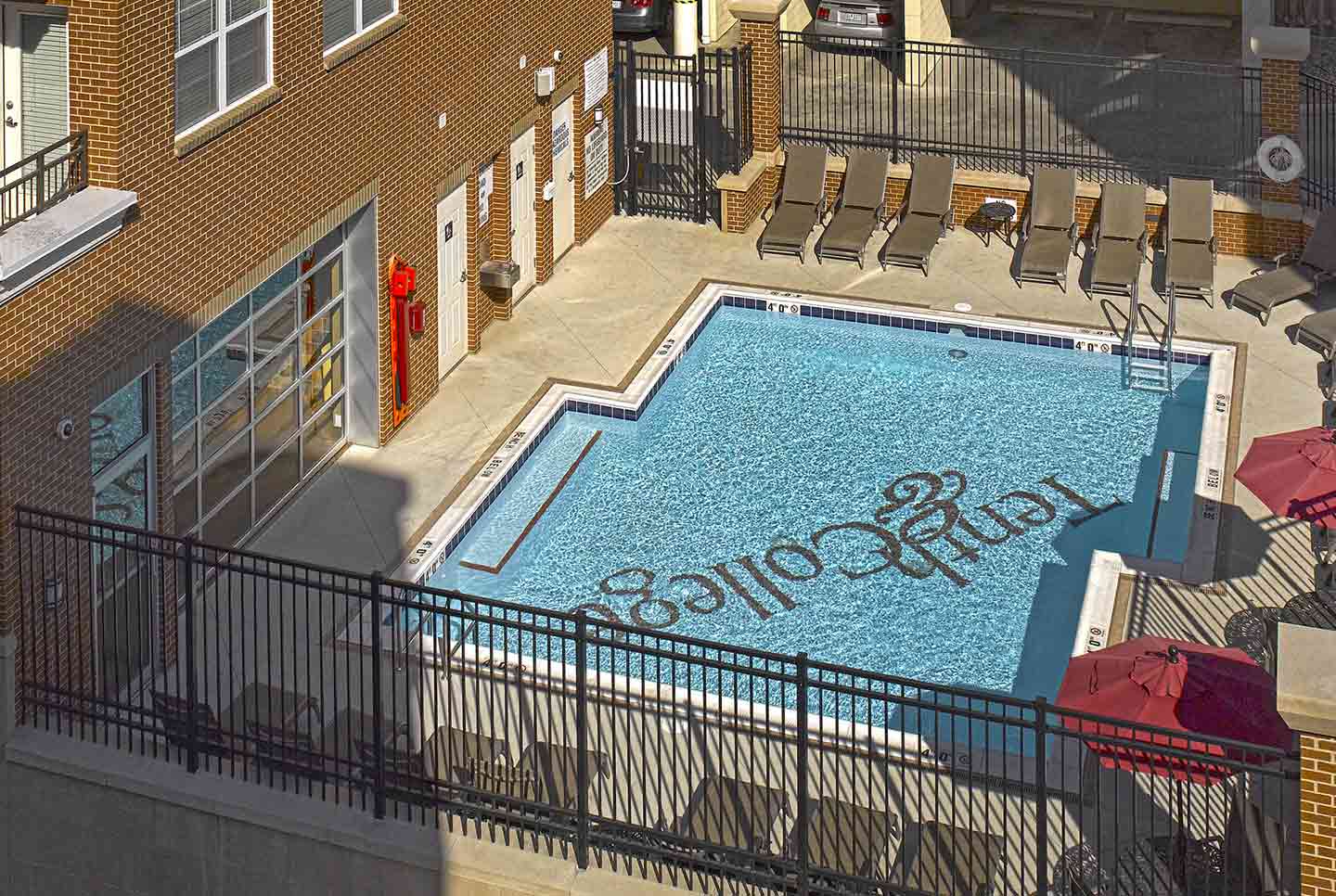 High-angle view of an outdoor swimming pool with the Tenth & College logo on the pool floor, surrounded by lounge chairs.